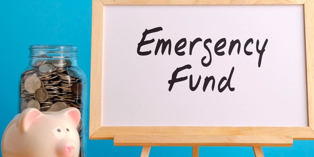 A piggy bank beside a whiteboard that reads “Emergency Fund”.
