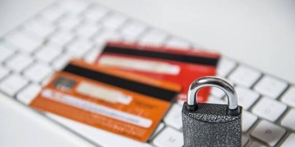 A close-up of two bank cards placed on a computer keyboard with a padlock in front, showing card security and fraud protection.